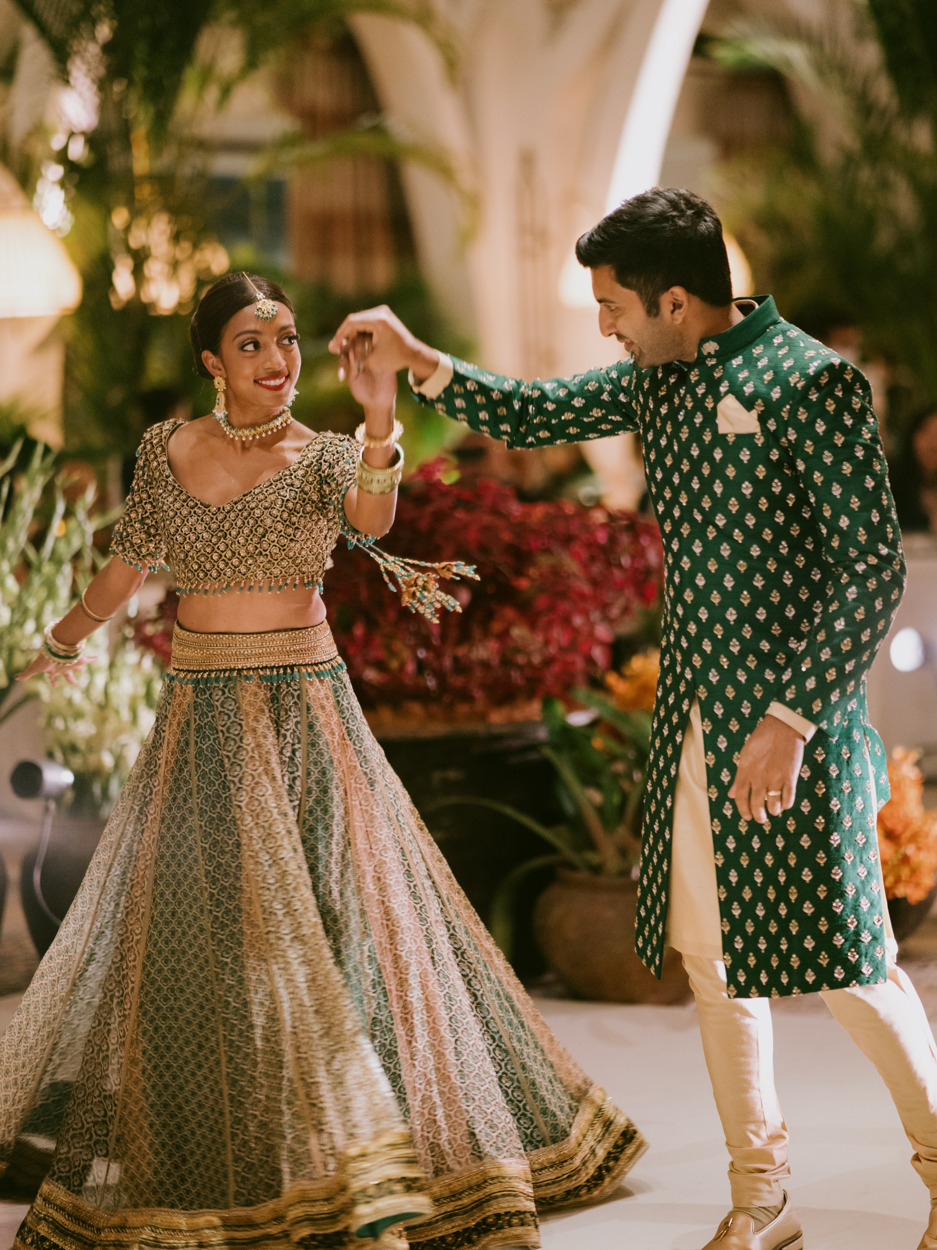 A couple dancing at a warmly lit reception surrounded by tropical planting