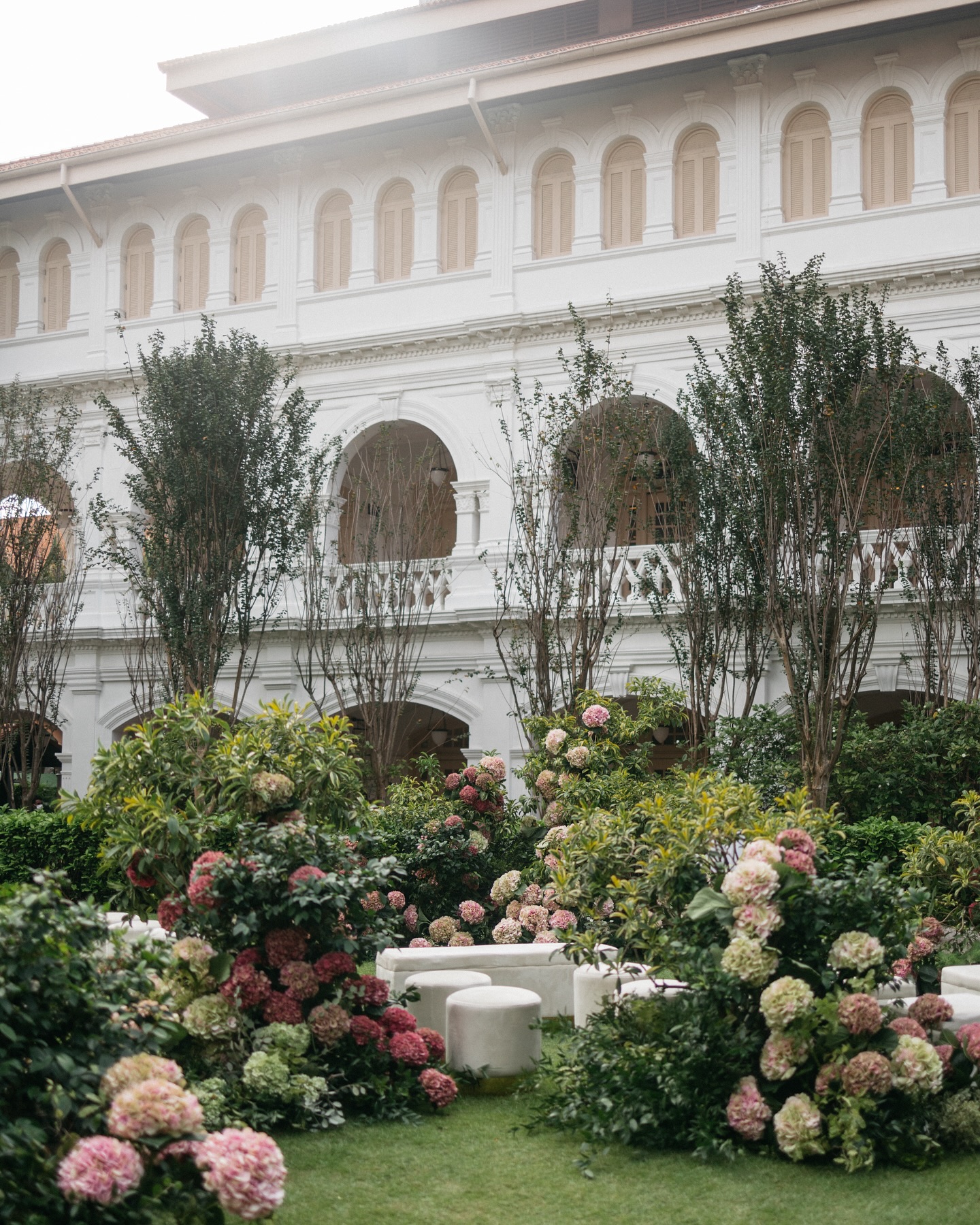 A colonial white facade above a garden of pink and green hydrangea with pale stone seating