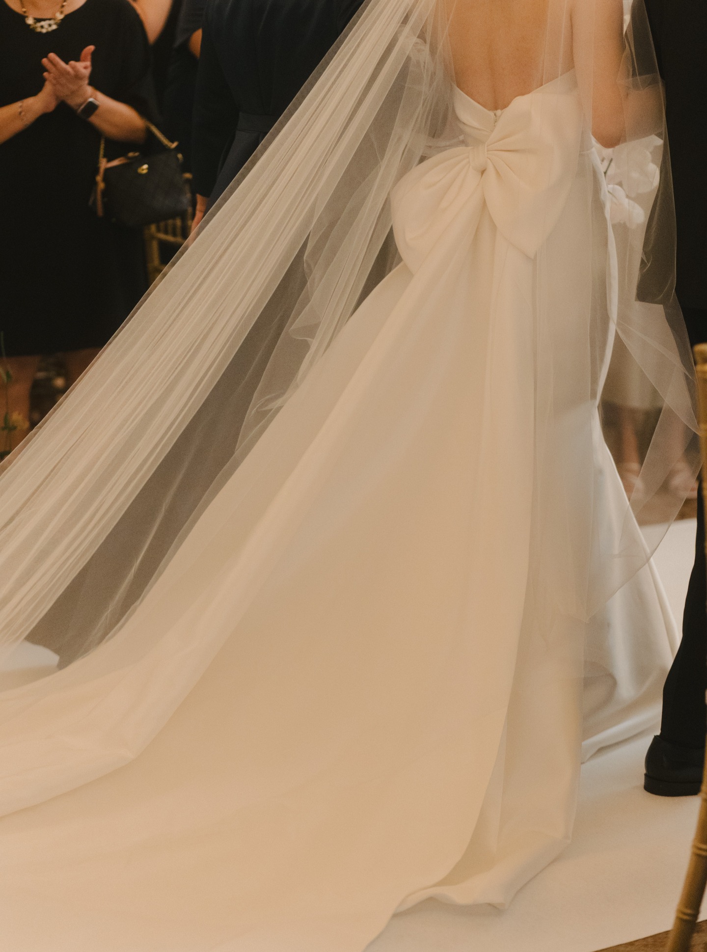 A bride at the altar, the long train of her gown fanned across the floor beneath a sculpted bow